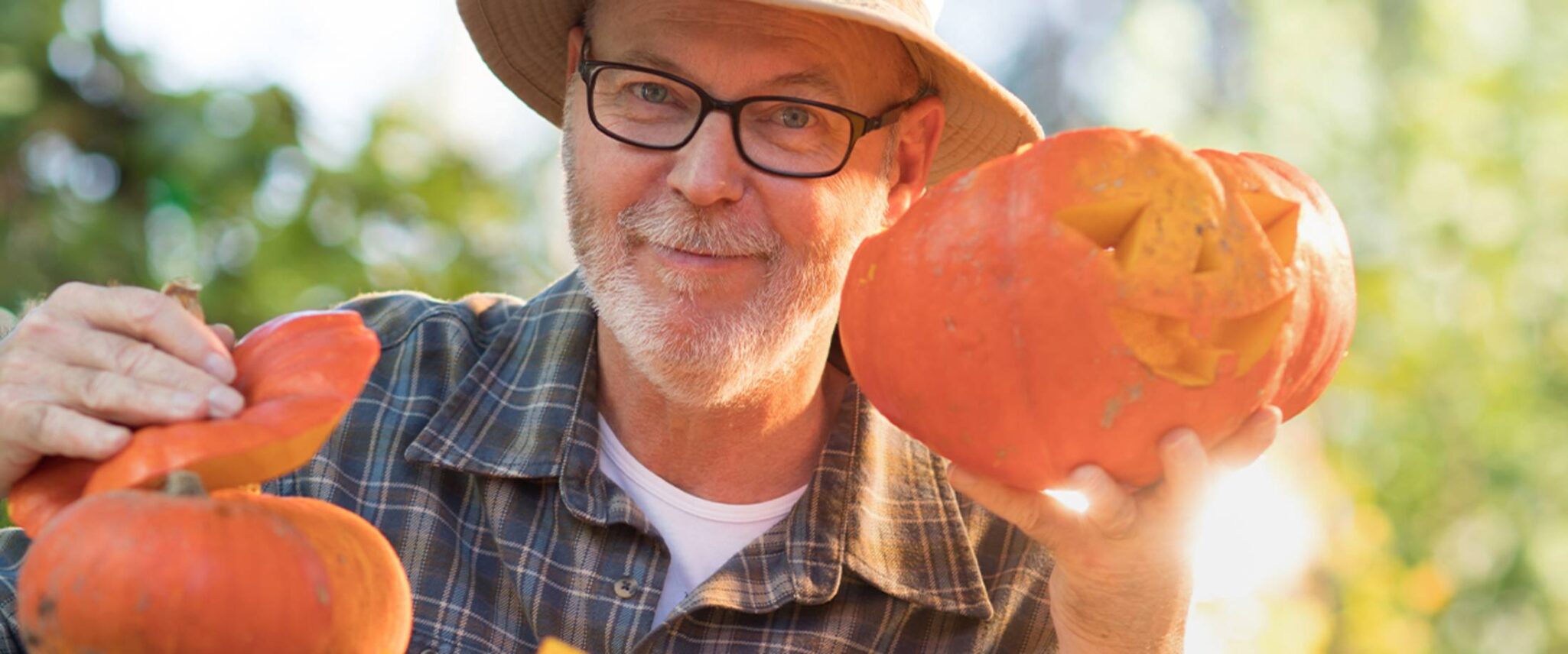 senior man holding up a pumpkin and jack-o-lantern