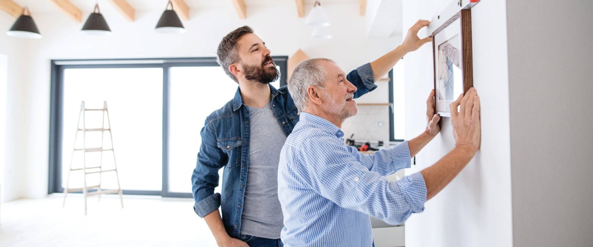 Senior man hanging up picture with son