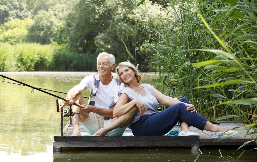 senior couple sitting at pier while fishing lakeside