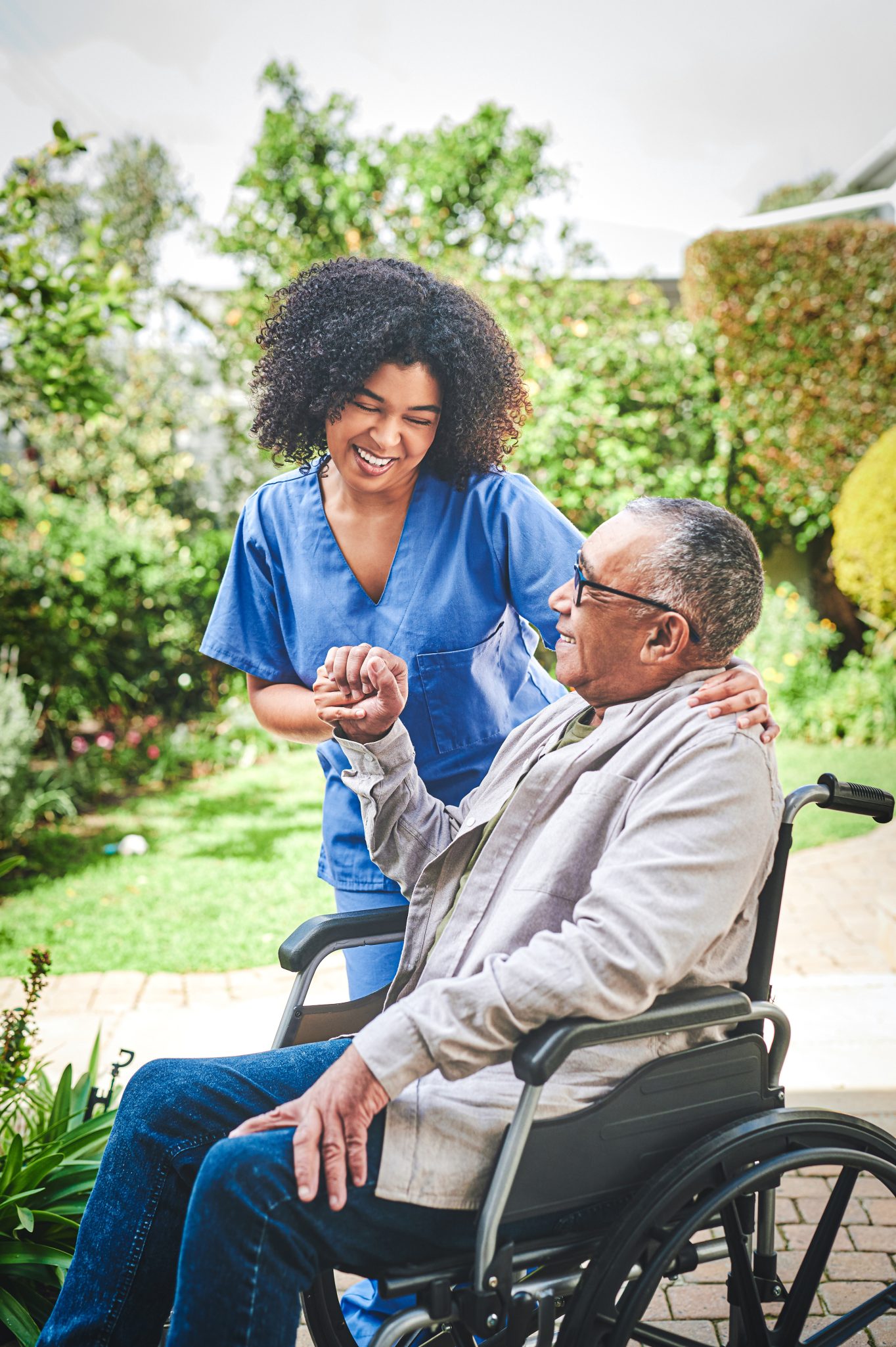 Female healthcare worker assisting senior male in wheelchair on outdoor walk