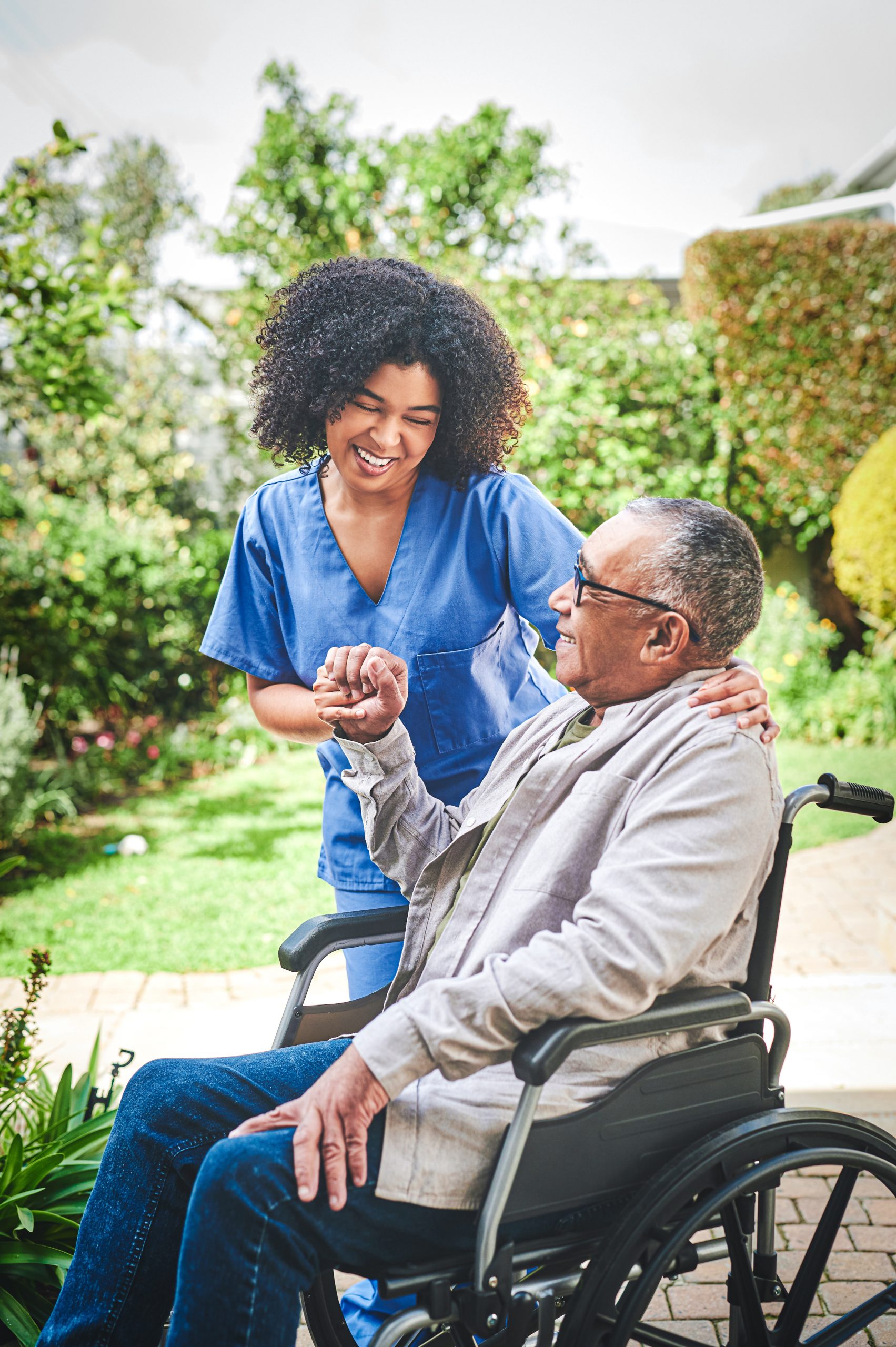 Female healthcare worker assisting senior male in wheelchair on outdoor walk
