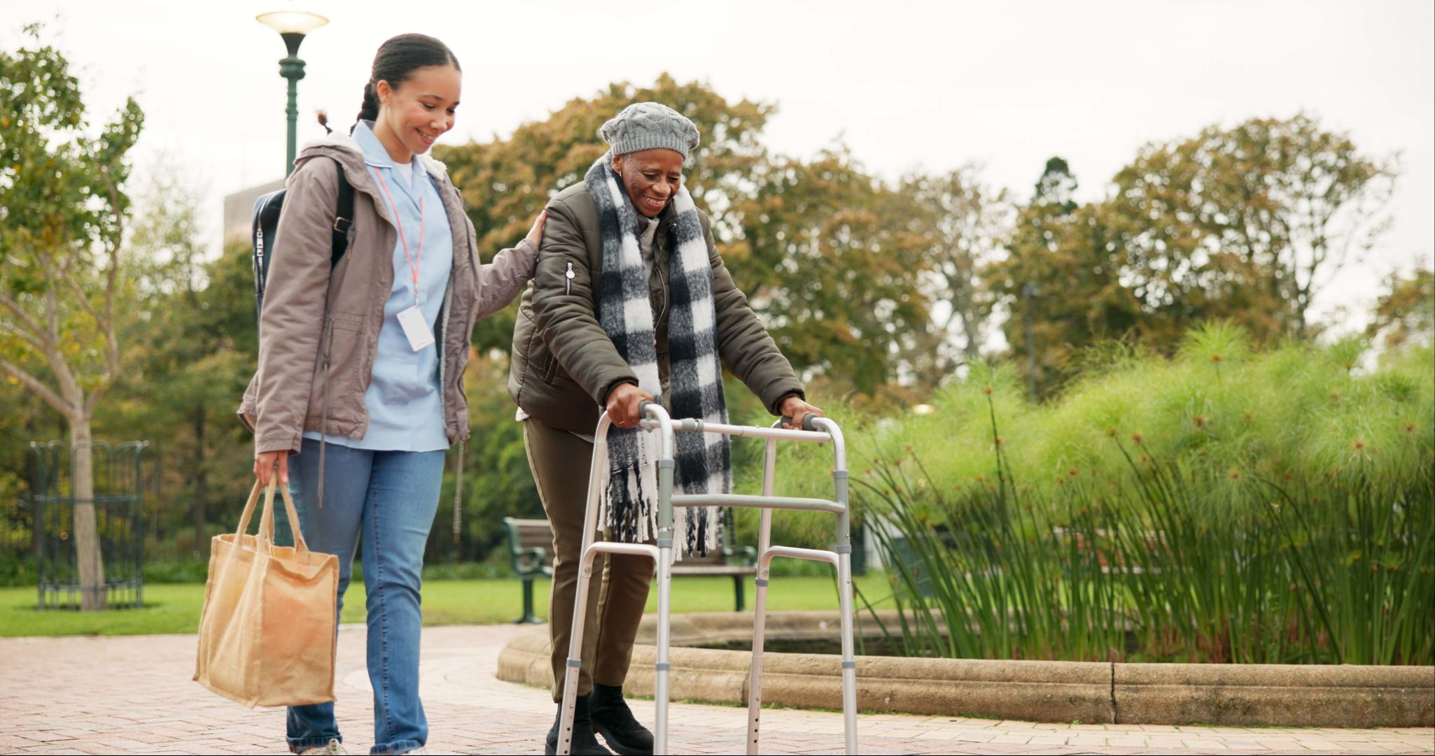 Female nurse assisting senior woman with walker on outdoor walk