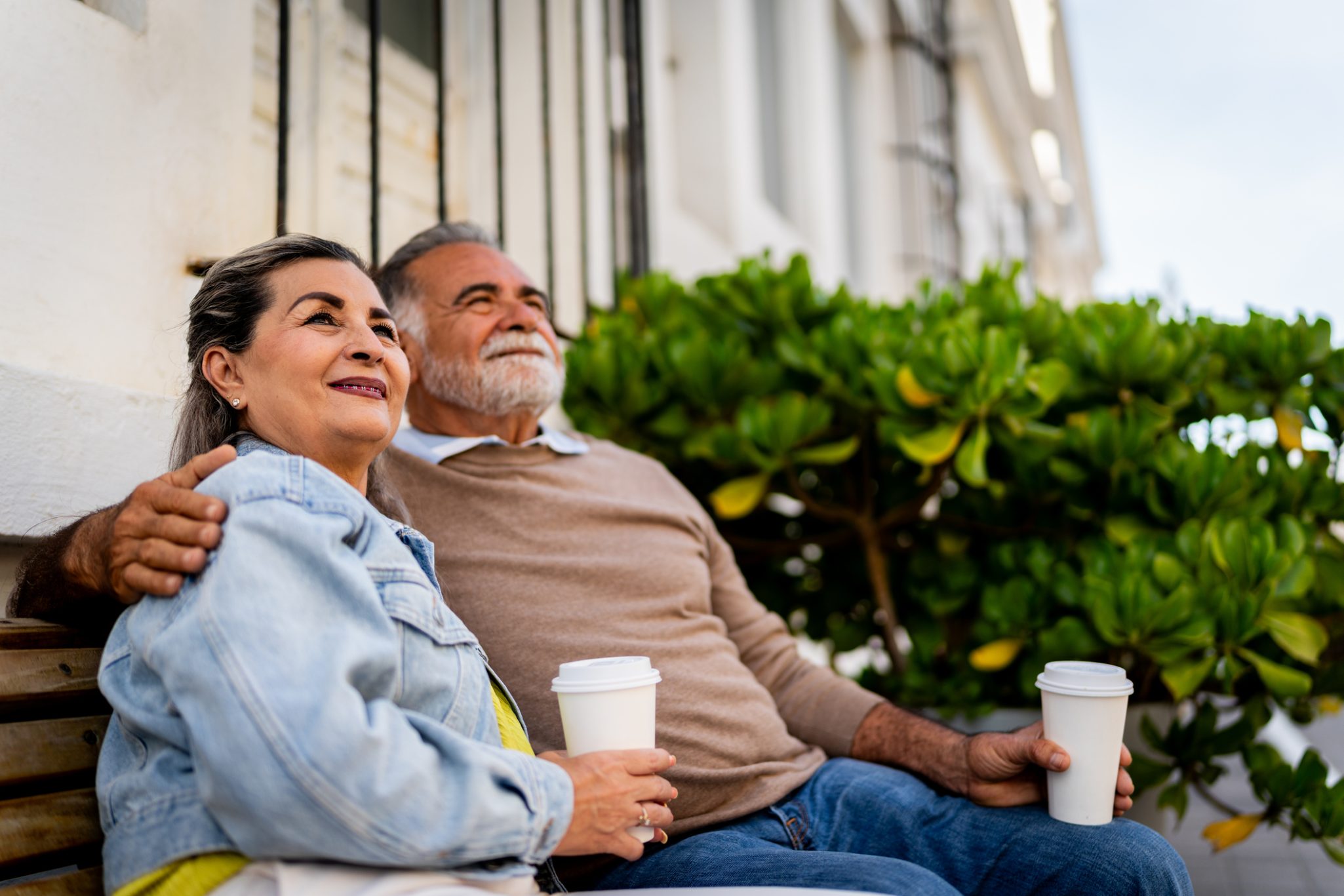 Smiling senior couple holding cups of coffee while sitting outside