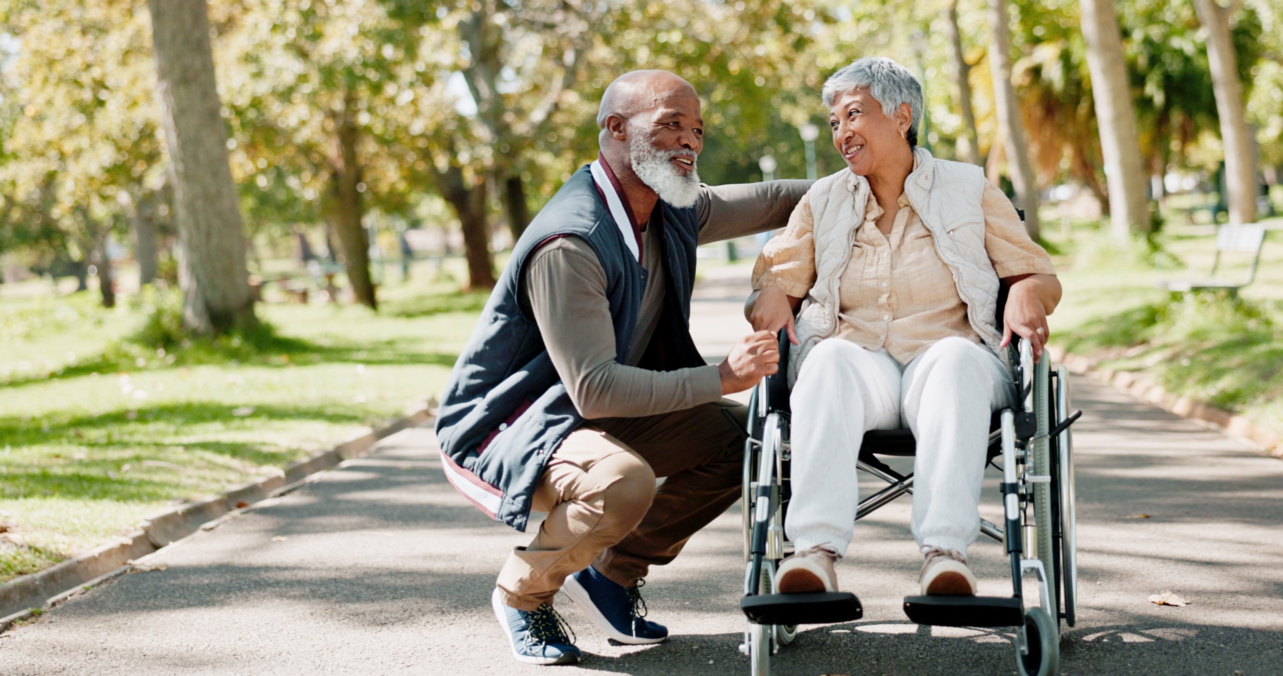 Senior man talking to senior woman in wheelchair on outdoor walk