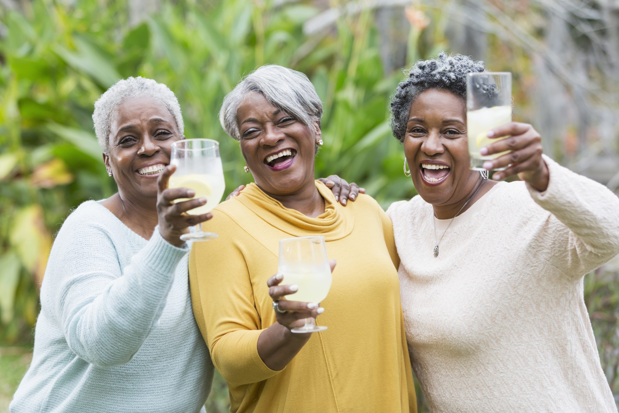Three smiling senior women holding up glasses of lemonade